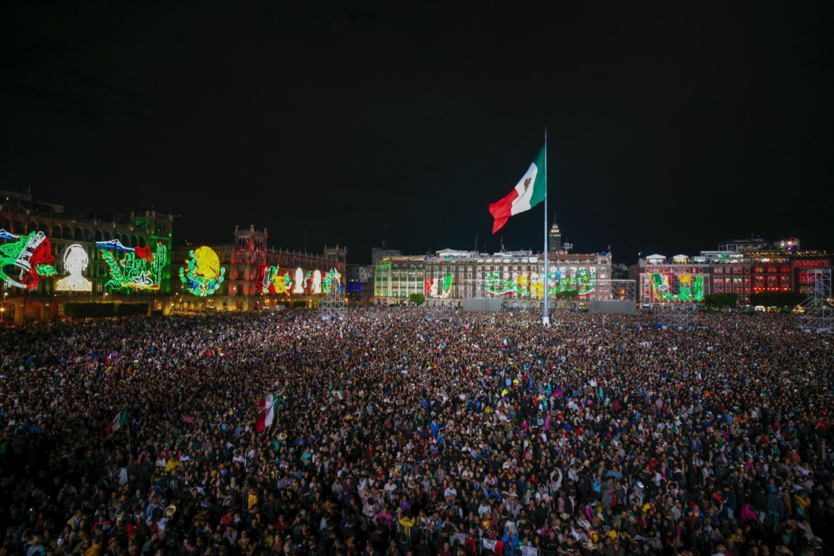 Una vista panorámica impresionante del Zócalo capitalino, lleno de miles de personas que ondean banderas y disfrutan del espectáculo de luces y adornos patrios.